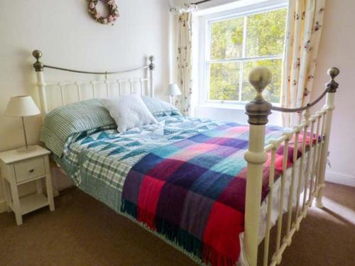 a bedroom with a bed with a striped blanket and a window at Woodside Cottage in Snainton
