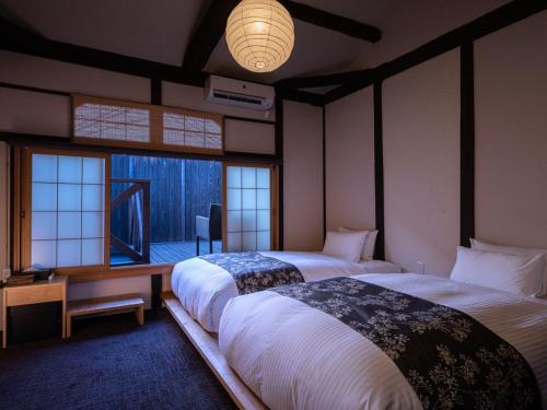 a bedroom with two beds and a desk and windows at Nazuna Kyoto Nijo-jo in Kyoto