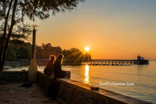 twee mensen die op een muur zitten te kijken naar de zonsondergang bij Issara Beach Resort in Sichon