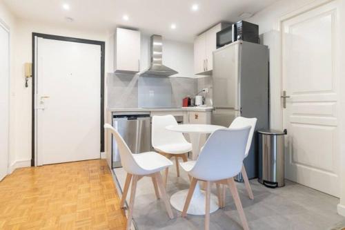 La cuisine est équipée de chaises blanches, d'une table et d'un réfrigérateur. dans l'établissement Cœur 16eme, standing et calme, à Paris