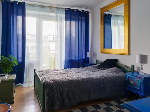 One&Only Saska Kępa Apartment في وارسو: غرفة نوم مع ستائر زرقاء وسرير ومرآة