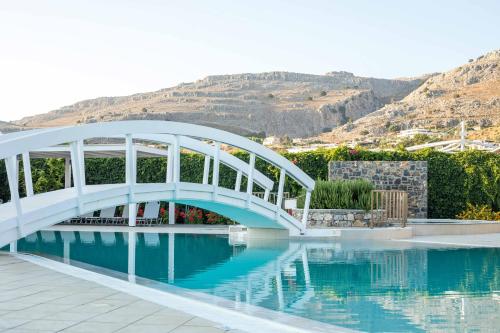 a white bridge over water with a mountain in the background at Lindos White Hotel & Suites in Líndos