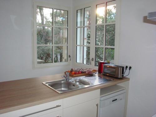 uma cozinha com um lavatório, um micro-ondas e 2 janelas em Maison basque dans les pins, au calme, 200m plage em La Baule