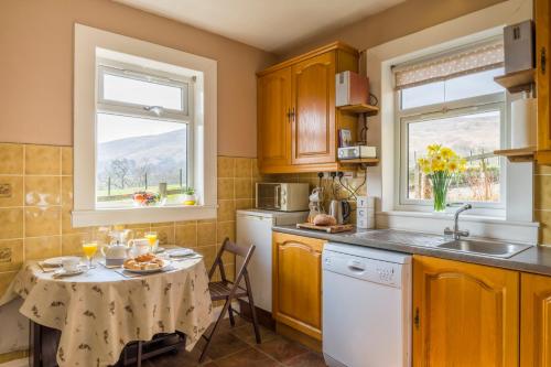 a kitchen with a table and a sink and two windows at Shemore Farm Holiday Cottage in Luss
