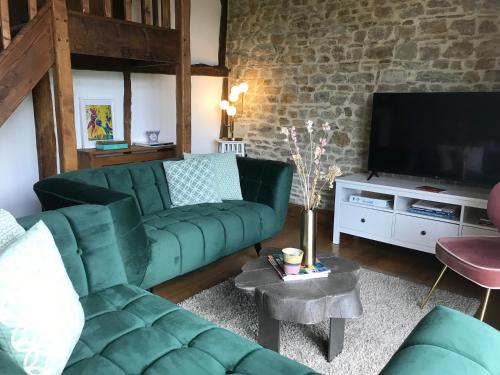 een woonkamer met een groene bank en een tv bij La Paix, Gîte bucolique en Normandie in Condé-sur-Noireau