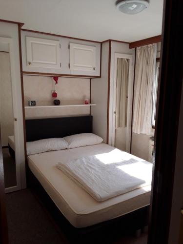 een kleine slaapkamer met een bed met witte lakens bij Marina beach chalet nummer P0 28 in Hoek