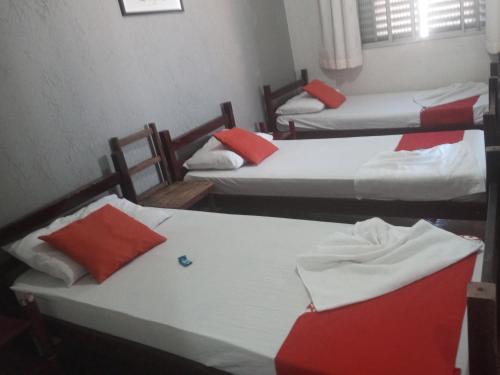 a room with three beds with red and white pillows at Hotel Central in Jacareí