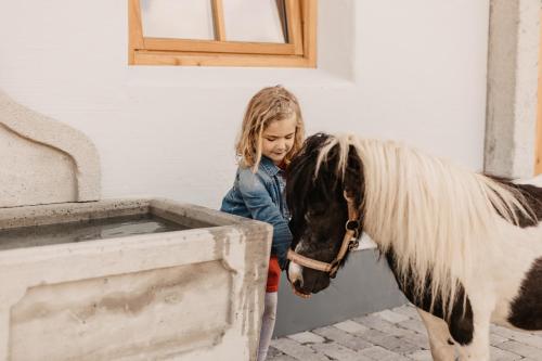 mała dziewczynka stojąca obok konia i patrząca na koryto w obiekcie Gut Berg Naturhotel w mieście Sankt Johann im Pongau