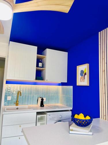 uma cozinha azul com armários brancos e uma taça de fruta em Flore em Le Grau-du-Roi
