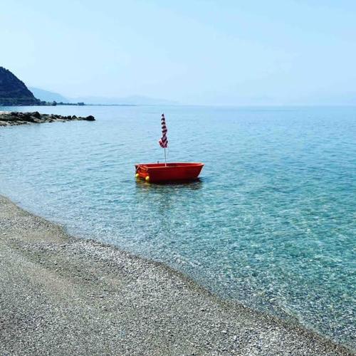 a red boat sitting in the water on a beach at KRATHIS APARTMENTS ΜΕΓΑΛΟ in Paralía Platánou