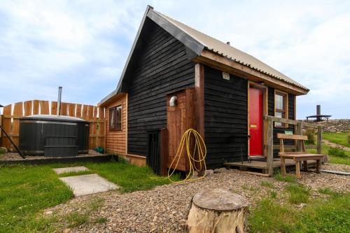 a small black house with a red door at Shepherd's Loch Glamping in Turriff