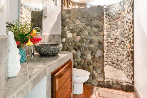 a bathroom with a toilet and a stone wall at Villas Oasis in Manuel Antonio