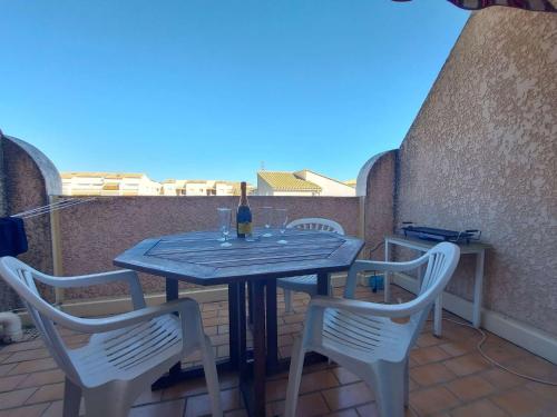 - une table avec des chaises et une bouteille de vin sur le balcon dans l'établissement Studio Cabine avec Terrasse, Piscine et Parking Privé à Marseillan - FR-1-326-774, à Marseillan