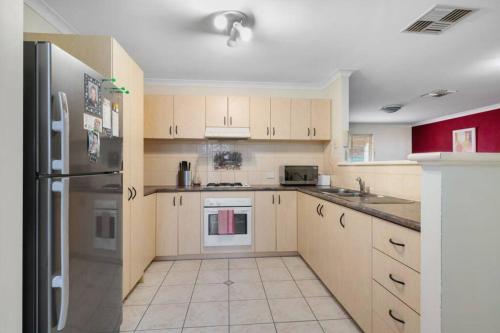 a kitchen with white cabinets and a stainless steel refrigerator at Adorable-secure 3 bedroom holiday home with Pool around the corner from The Miners Rest. in Kalgoorlie