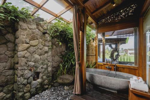 a bathroom with a stone wall and a tub at Airsania Ubud Antique Villas in Ubud