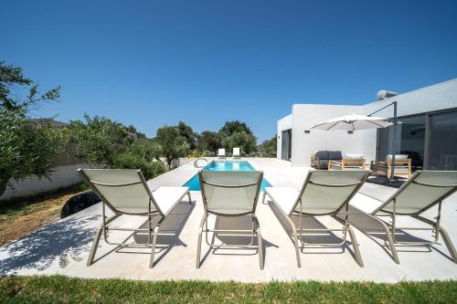 a group of chairs and a table with an umbrella at Villa Vivian Heated Private Swimming Pool & Jacuzzi in Georgioupolis