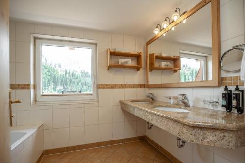a bathroom with two sinks and a mirror and a tub at Moseralm Dolomiti Spa Resort in Nova Levante
