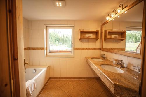 a bathroom with two sinks and a tub and a window at Moseralm Dolomiti Spa Resort in Nova Levante