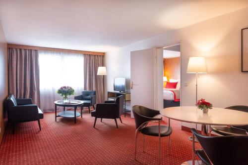 a hotel room with a table and chairs and a bed at Le M & Spa Bordeaux Aéroport by Hôtels & Préférence in Mérignac