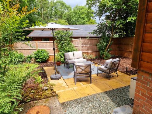 a patio with a table and chairs and an umbrella at Wnion Wood Lodge with log burner & sauna in Snowdonia in Llanfachreth