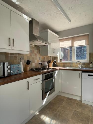 een witte keuken met witte kasten en een raam bij Drake Cottage - riverside retreat, Jackfield, Ironbridge Gorge, Shropshire in Coalport