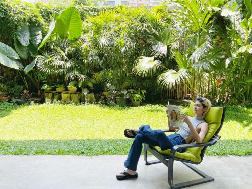 a woman sitting in a chair reading a book at Lamphu House Chiang Mai in Chiang Mai