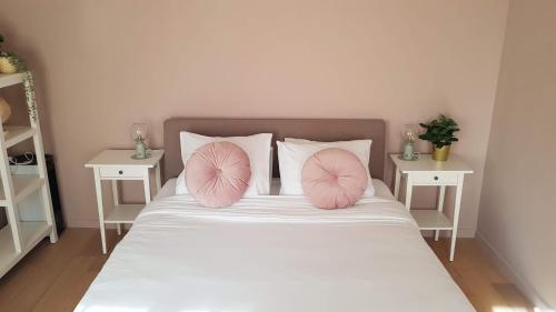 een wit bed met roze kussens en 2 tafels bij BnB Antwerpen - CHIQUE in Antwerpen