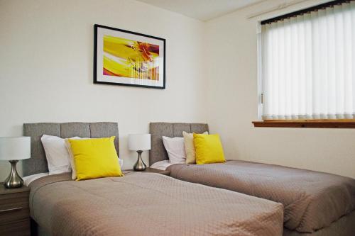 two beds with yellow pillows in a bedroom at Superb 2 Bedroom Flat in Inverness