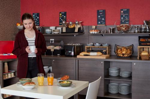 a woman standing in a kitchen holding a cup of coffee at Aparthotel Adagio Access Poitiers in Poitiers