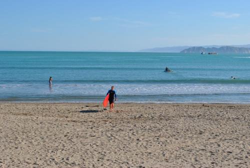 a person standing on a beach holding a surfboard at Waikanae Beach TOP 10 Holiday Park in Gisborne