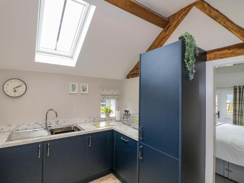 cocina con armarios azules y techo con ventana en The Stables, en Whiston