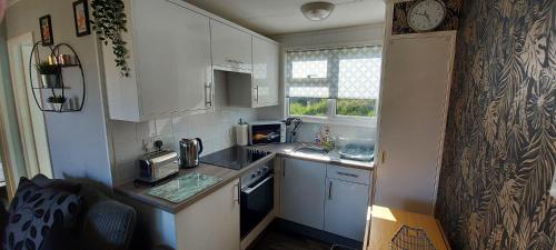 a small kitchen with white cabinets and a clock on the wall at Rosehill Beach in Hemsby