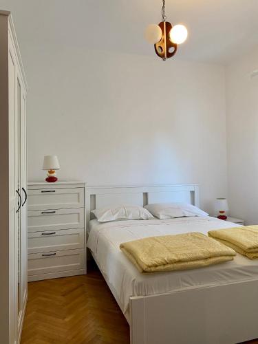a white bedroom with a bed and a dresser at Apartmani Luka in Korčula
