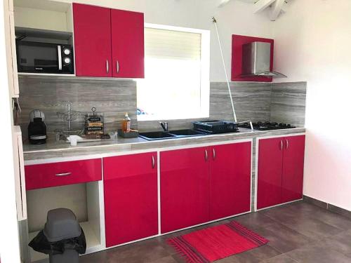 a kitchen with red cabinets and a sink and a window at Villa enchanteresse au Moule avec piscine privée in Le Moule