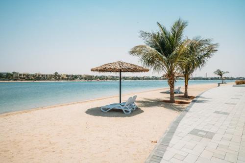 a beach with a chair and an umbrella and palm trees at Relaxing villa with access to pool and beach in Ras al Khaimah