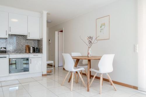 a white kitchen with a wooden table and white chairs at Minusio Apartment by Quokka 360 - bright and modern flat with balcony in Minusio