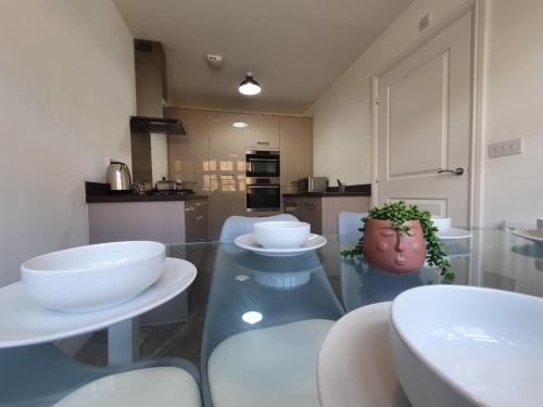 una cucina con tavolo in vetro e sedie bianche di Cheerful 4 - Tranquil Oasis Modern and Spacious Retreat 4-Bedroom with Private Parking and Serene Gardens a Luton