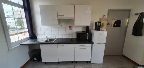 uma cozinha com armários brancos e um frigorífico em f2 avec terasse sud ouest em Dunkerque