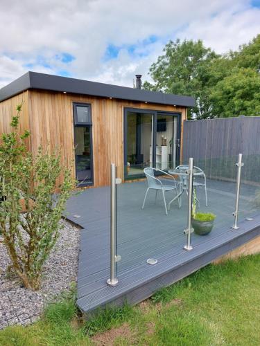 a wooden deck with a table and a chair on it at The Den - Modern cabin with wood burning stove in Ludchurch