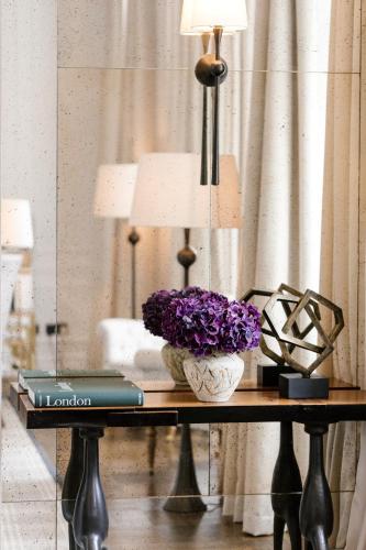 a table with a lamp and a vase of purple flowers at The Adria in London