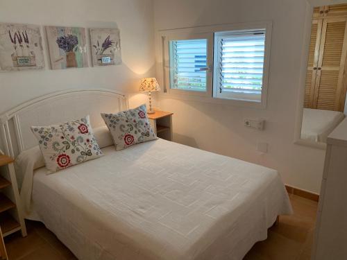 a bedroom with a white bed with two pillows at Casa Carmencita, immersa nel verde a pochi passi da mare in Es Caló