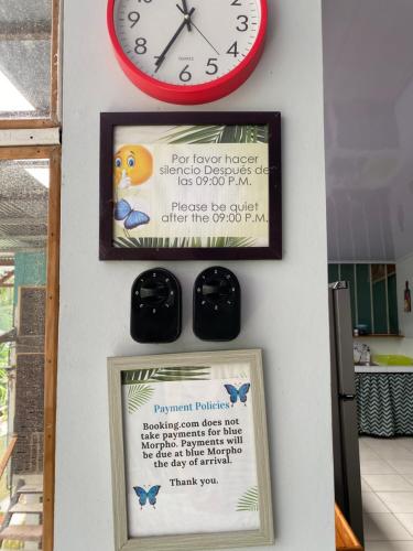 a clock and a sign on a wall with a picture at Blue Morpho House B&B in Manuel Antonio