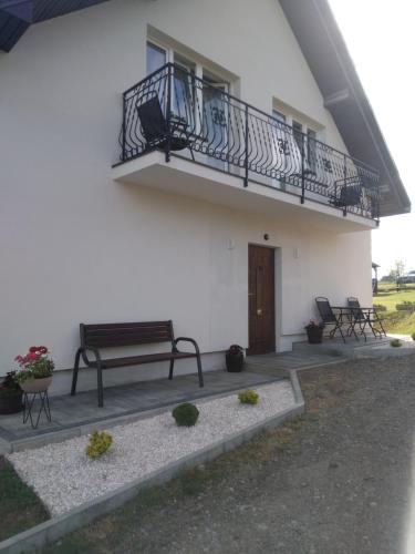 a white building with a balcony and a bench at Noclegi U Janusza 536-310-384 in Polańczyk