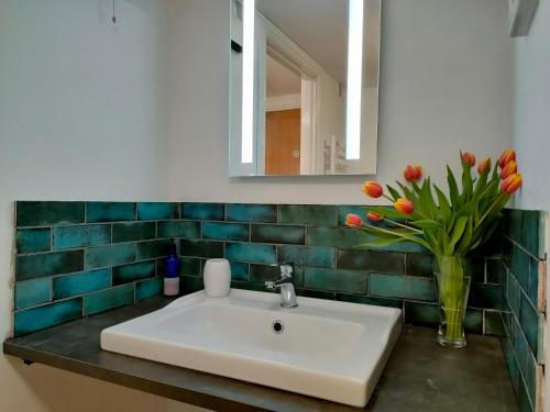 a bathroom sink with a vase of tulips and a mirror at The Old Bakery Seahouses in Seahouses