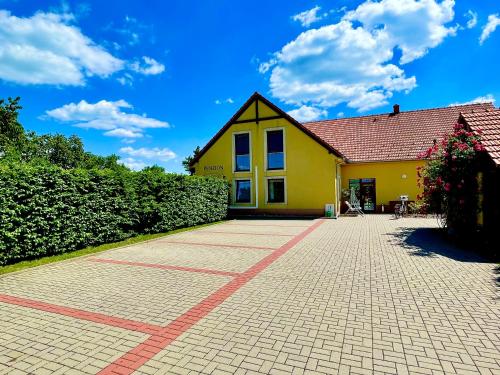 a yellow house with a red roof and a brick driveway at Penzion Sarton in Lukov