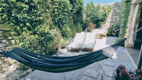 a hammock in a garden with two benches at Rector's Villa - Charming Retreat in Old Town with Jacuzzi in Private Courtyard in Rab