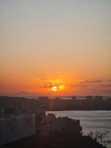 um pôr-do-sol sobre a água com edifícios e uma cidade em Casa Mar da Grécia em Arraial do Cabo