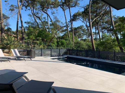 une terrasse avec une piscine, des chaises et des arbres dans l'établissement Villa Aréna à Labenne-Océan, à Labenne