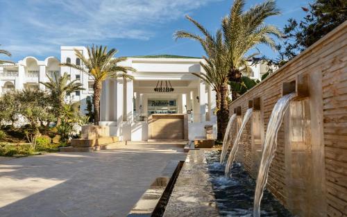 a white building with palm trees in front of it at Radisson Blu Resort & Thalasso Hammamet in Hammamet