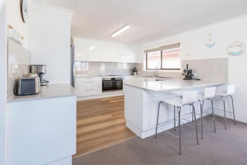 a white kitchen with a counter and stools at Waterfront on Forster Keys in Forster